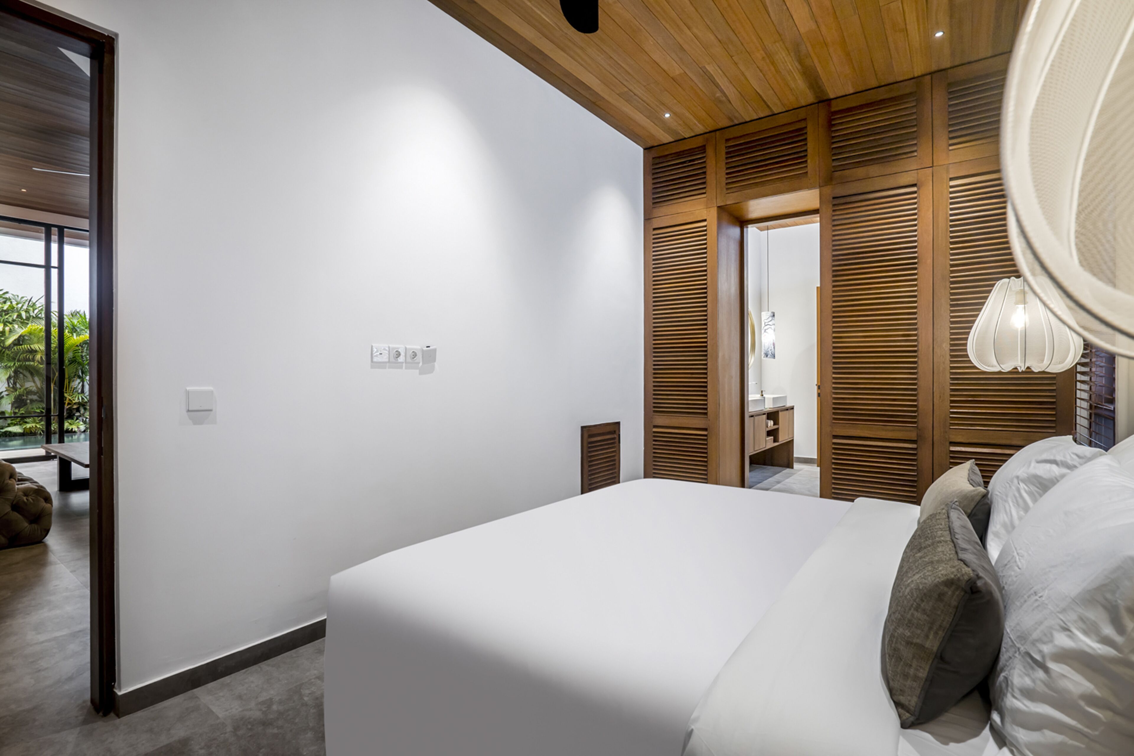 Een moderne slaapkamer met een groot bed, houten lambrisering en uitzicht op een tuin.