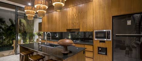 Una cucina moderna con mobili in legno, un'isola centrale con sgabelli, elettrodomestici in acciaio inossidabile e illuminazione a sospensione.