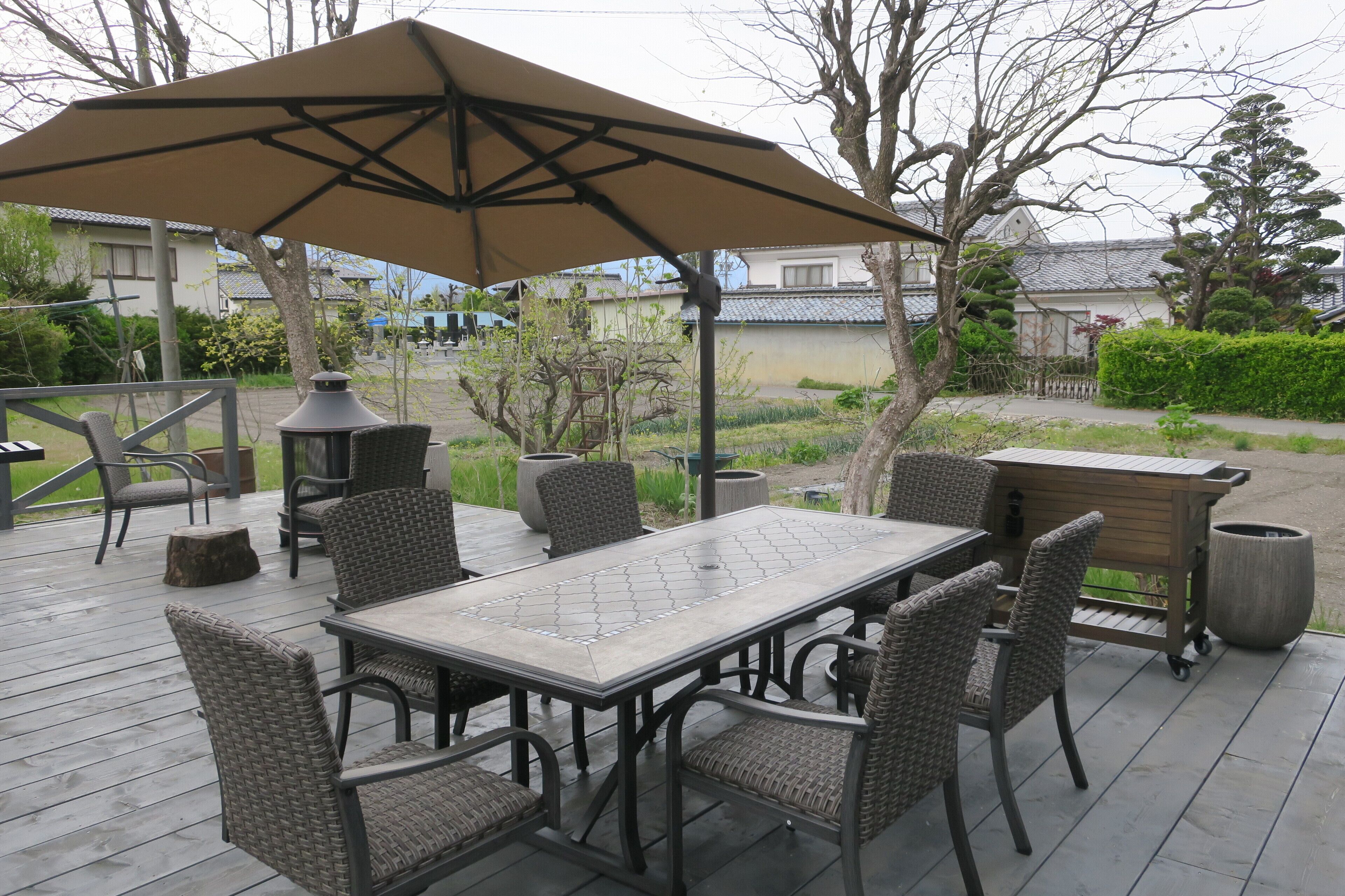 Eine Terrasse im Freien mit Tisch, Stühlen, einem großen Sonnenschirm und einem Grill.