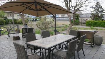 Eine Terrasse im Freien mit Tisch, Stühlen, einem großen Sonnenschirm und einem Grill.