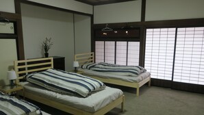 A room with two wooden beds, each with striped bedding and a bedside table with a lamp. There is a potted plant on the left and a large window with a view of the outside. - 5 minutes from Azumino Interchange! Ideal for families and groups staying together! A private old house that can accommodate up to 14 people in 5 bedrooms! Barbecue available on the terrace! (AZUMINO-CITY TOYOSHINA TAZAWA)