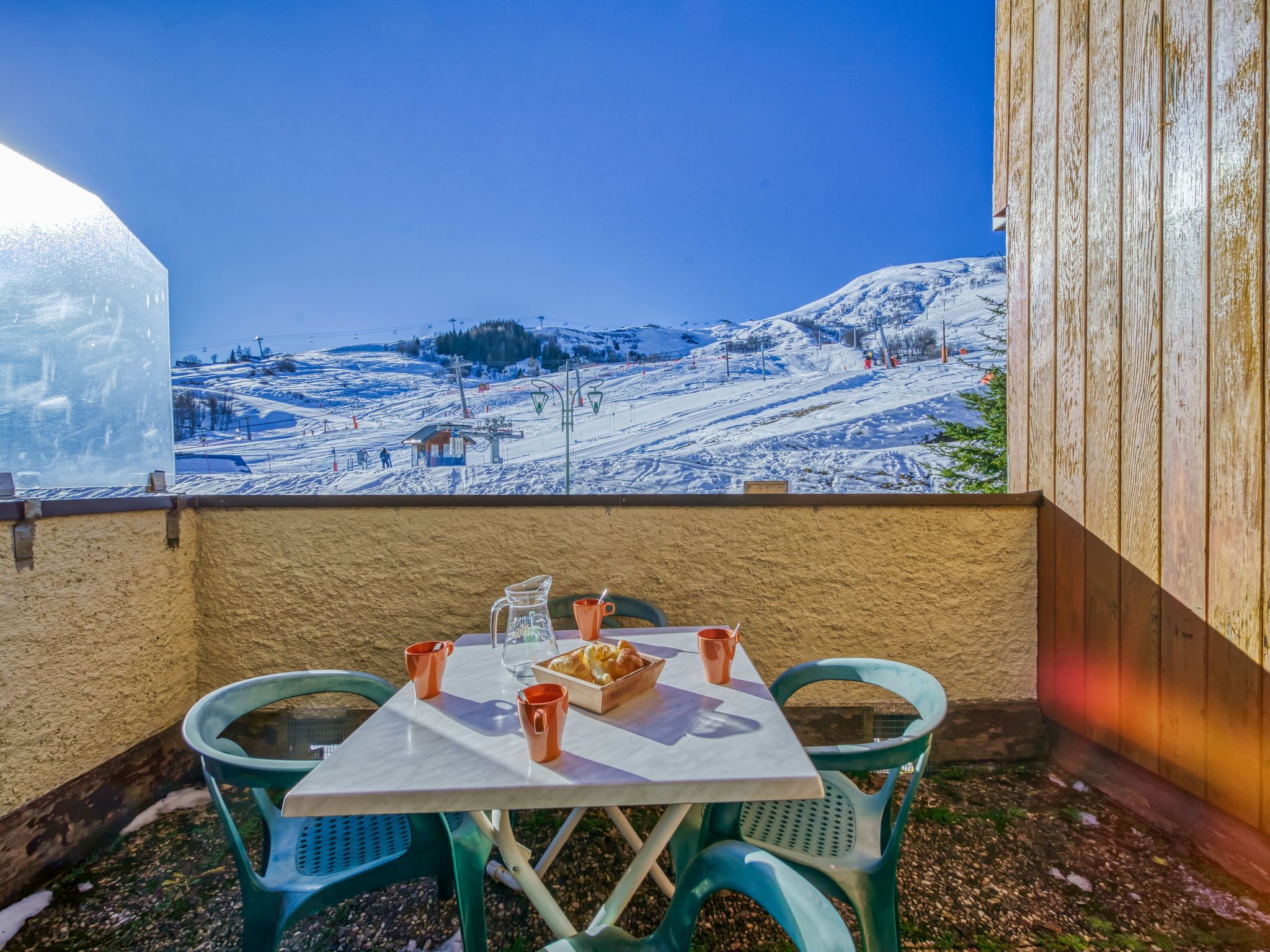 Una mesa con sillas y una vajilla en un balcón con vistas a un paisaje montañoso nevado.