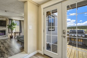 A room with a fireplace, a potted plant, a sofa, and a view of a deck with a grill. - Mighty Mobile (Palmer Lake)