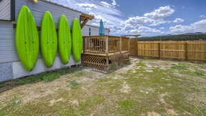 Una terraza de madera con valla de madera, un paraguas azul y tres tablas de surf verdes apoyadas contra un edificio.