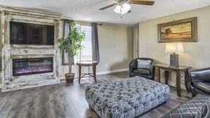 Una habitación con chimenea, ventilador de techo, cama, sillón y lámpara.