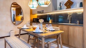 A dining area with a wooden table set for four, a bench, and a kitchen in the background. -  Villa Sorano Canggu by Nagisa Bali (Kerobokan)