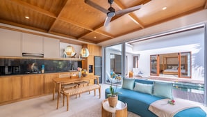 A modern kitchen with wooden cabinets, a dining area with a bench, and a blue sofa with a view of a pool. -  Villa Sorano Canggu by Nagisa Bali (Kerobokan)