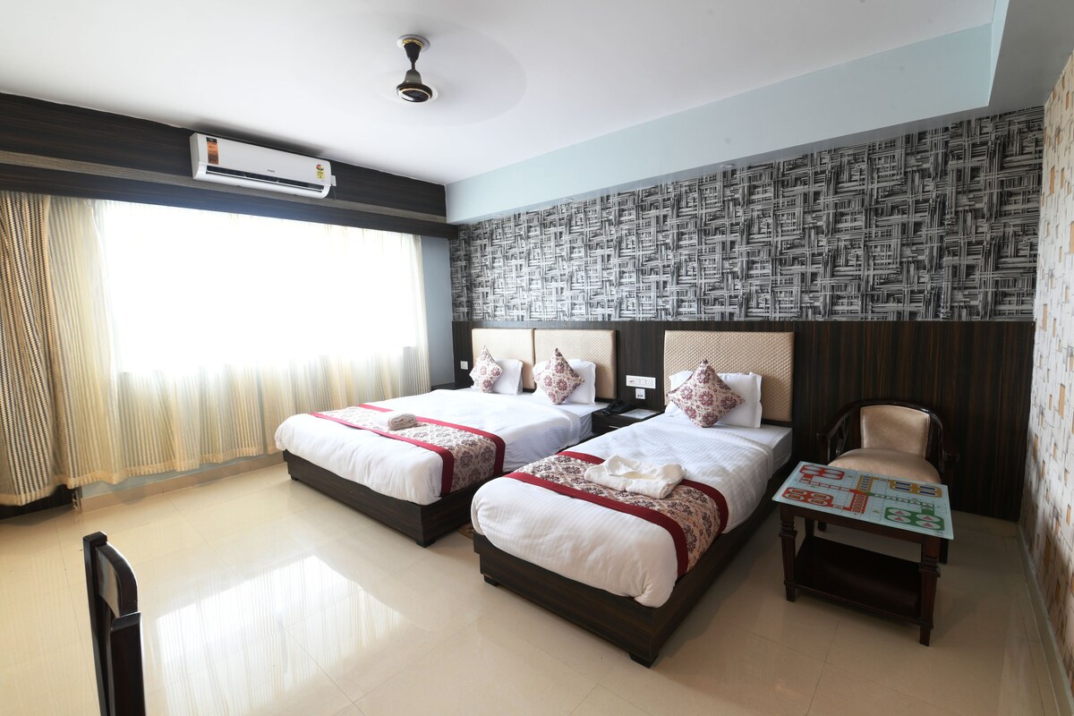 Une chambre d’hôtel avec deux lits, une petite table, une chaise et un ventilateur de plafond.