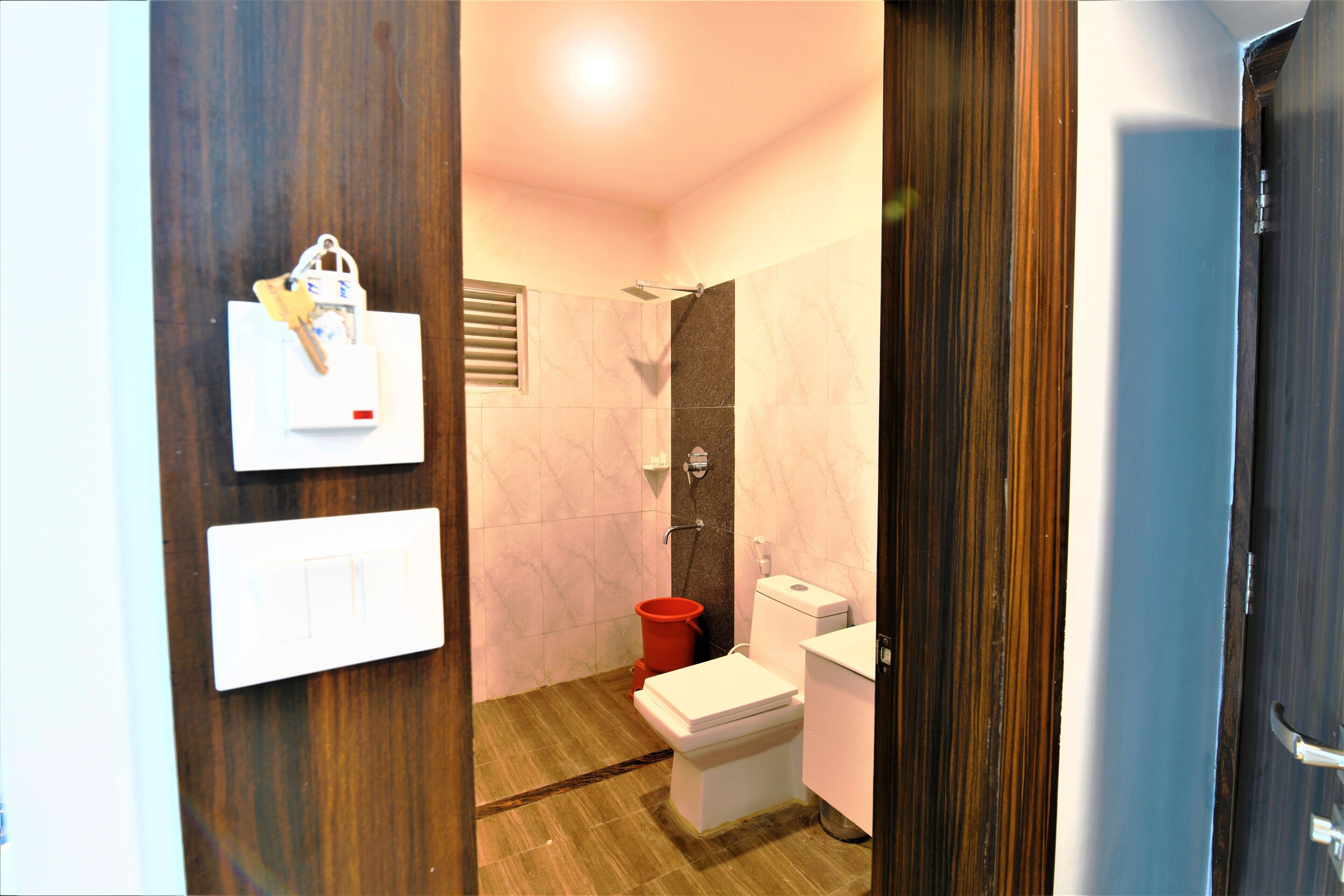 A bathroom with a toilet, a shower, and a red bucket.
