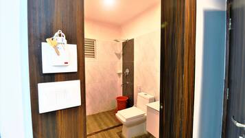 A bathroom with a toilet, a shower, and a red bucket.