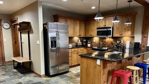 A kitchen with a stainless steel refrigerator, wooden cabinets, a microwave, and a granite countertop.