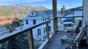 A balcony with a view of a snowy landscape, a wooden deck, and two reclining chairs.