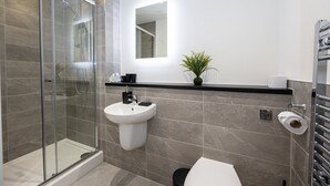 Une salle de bain moderne avec une douche à l’italienne en verre, un lavabo blanc et des toilettes.
