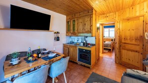A wooden interior with a dining table, chairs, a TV mounted on the wall, wooden cabinets, and a kitchen area with a stove. - Chaberton Romantic Retreat Ski In Ski Out, Claviere, Italy (Claviere)