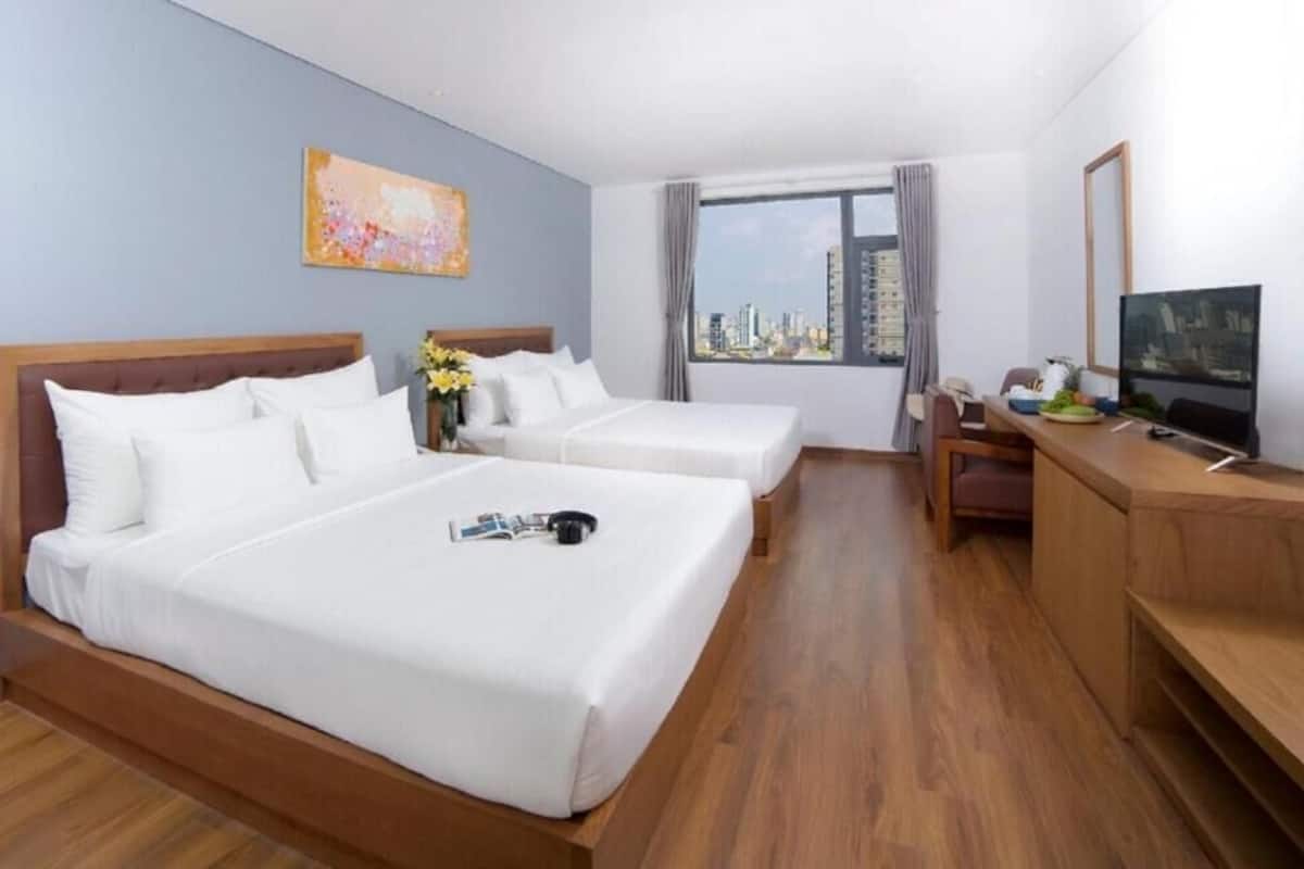 A hotel room with two beds, a desk with a TV, a window with a city view, and a painting on the wall.