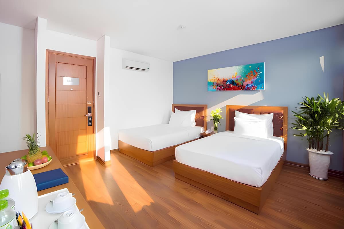 A hotel room with two beds, a wooden floor, a painting on the wall, and a potted plant.