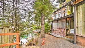 A wooden cabin with a glass door, surrounded by trees and a gravel path.