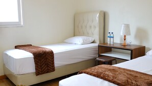 A hotel room with two single beds, a nightstand with a lamp, and a small table. - Bungo Bed Breakfast Workation (Bukittinggi)