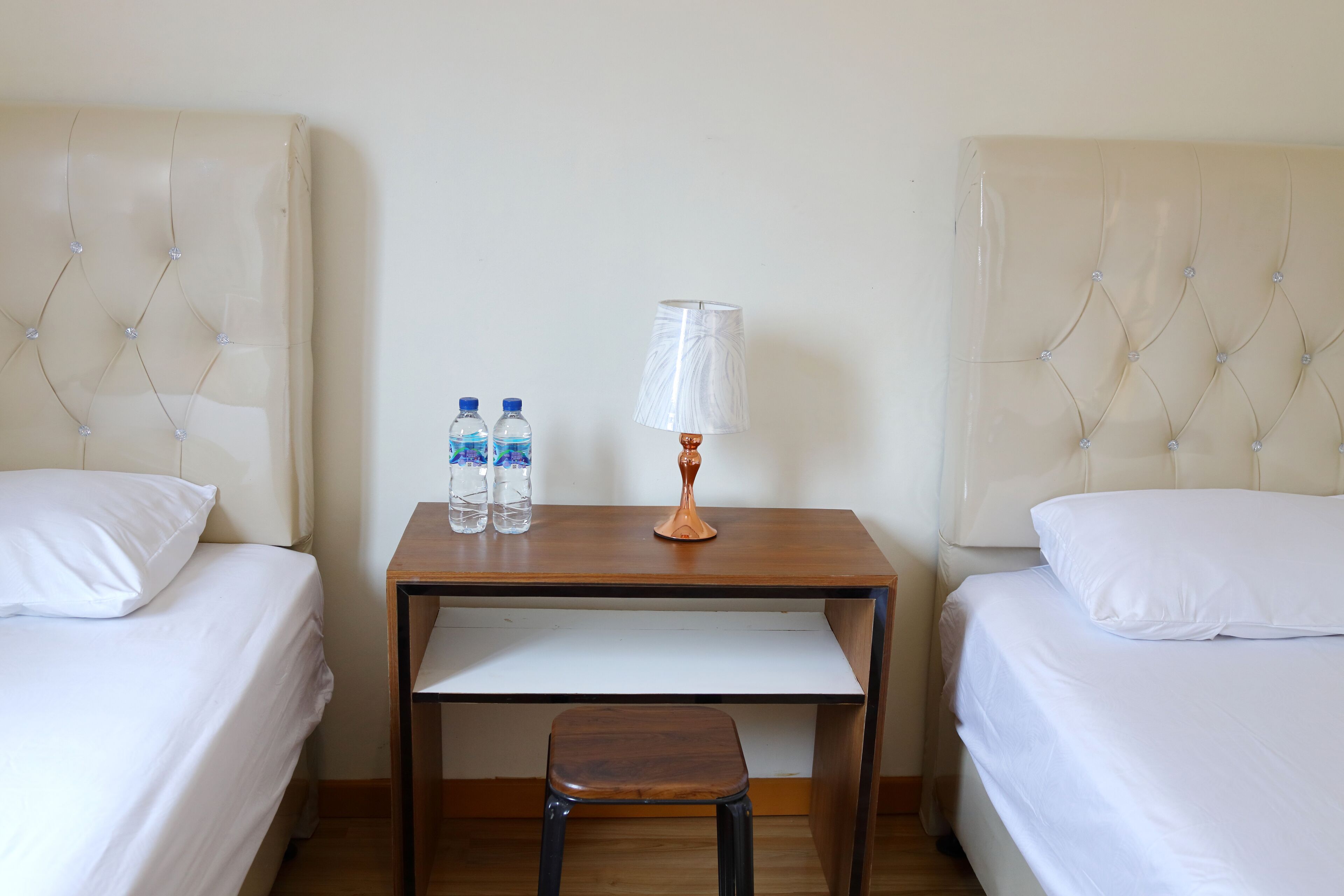 A hotel room with two beds, a small table with a lamp, and two water bottles.