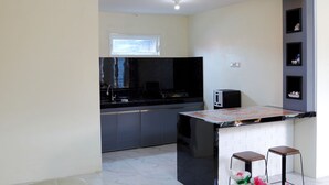A modern kitchen with dark grey cabinets, a black countertop, and a small island with stools. - Bungo Bed Breakfast Workation (Bukittinggi)