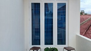 A balcony with two stools, a potted plant, and a white door with glass panels. - Bungo Bed Breakfast Workation (Bukittinggi)