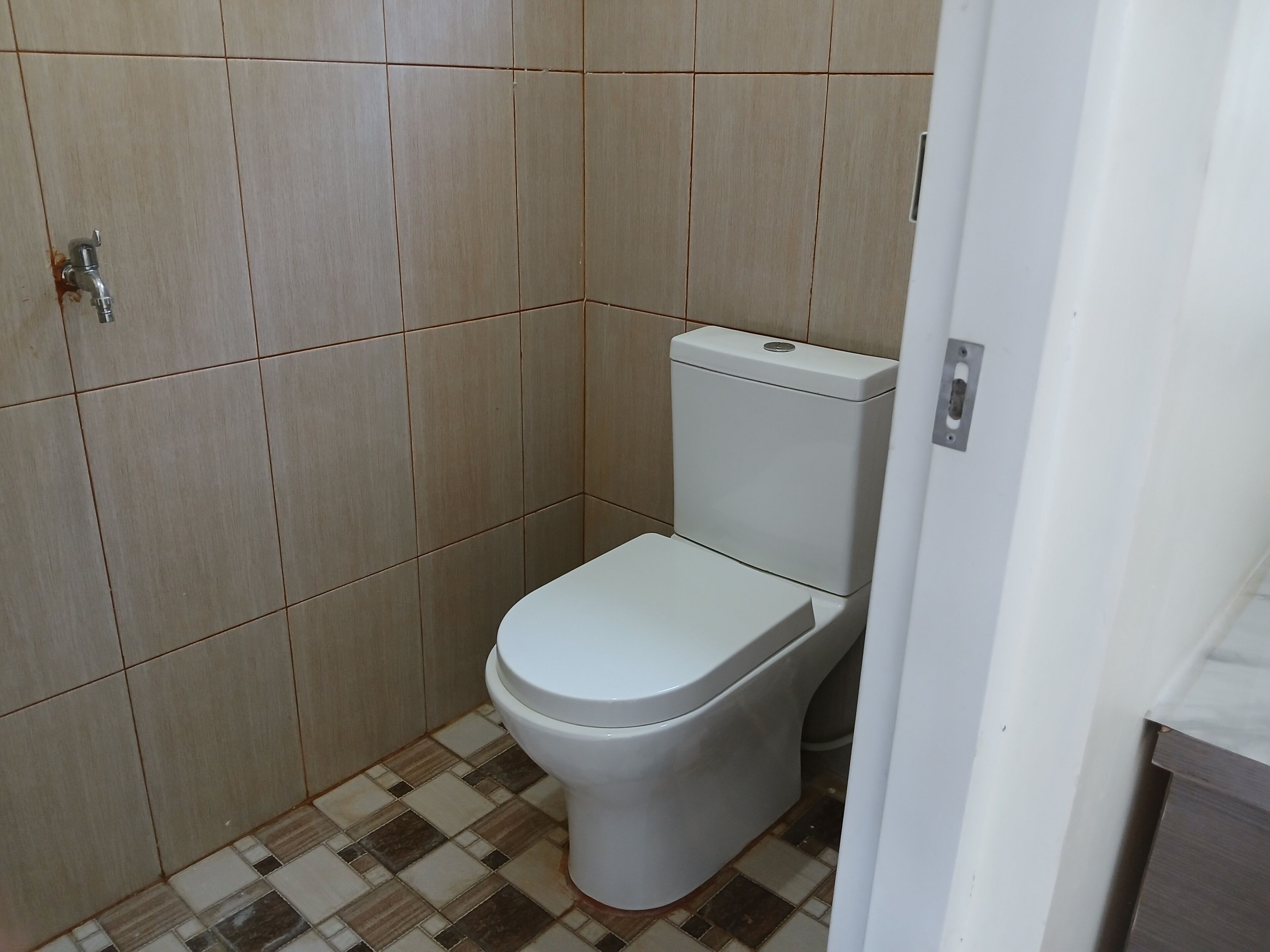 A small, clean bathroom with a toilet, tiled walls, and a checkered floor pattern.