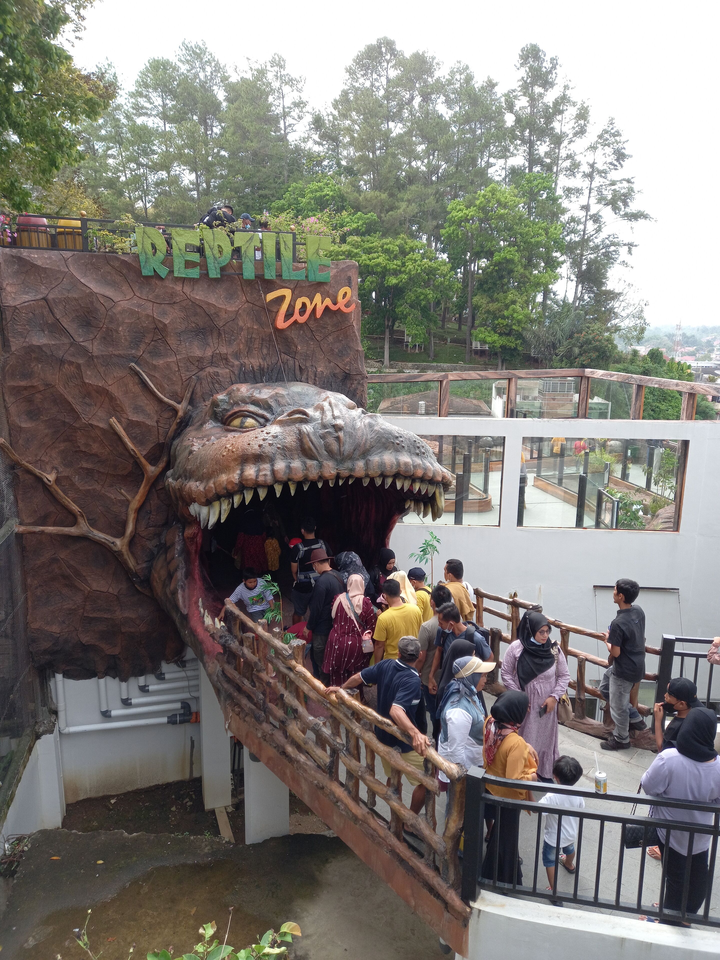 A group of people at a reptile zone with a large dinosaur sculpture.