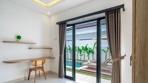 A modern room with a sliding glass door leading to a pool area, a wooden chair, and a small shelf with a plant. - Brand New Beautiful Stylish 2 BR Villa in Canggu (Bali)