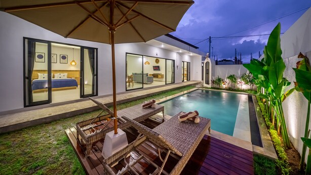 A modern poolside area with lounge chairs, a large umbrella, and a view of the interior. - Brand New Beautiful Stylish 2 BR Villa in Canggu (Bali)