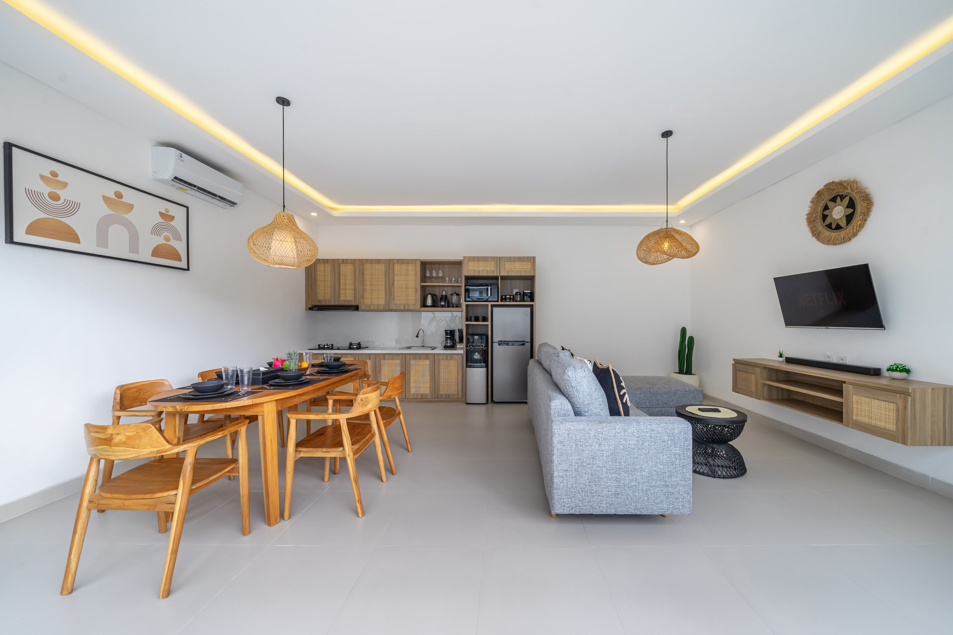 Una cucina moderna con mobili in legno, un'area pranzo con tavolo e sedie in legno, un divano grigio e una TV a schermo piatto su una mensola in legno.