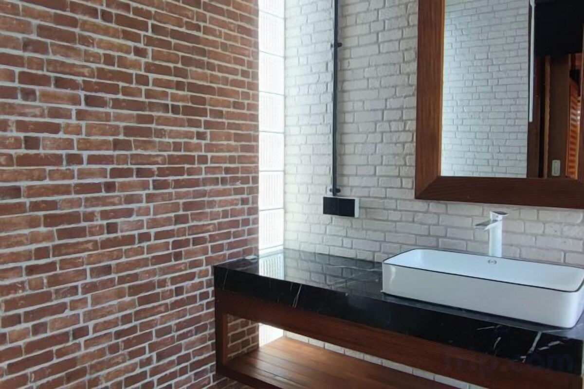 A bathroom with a brick wall, a white sink, and a wooden bench.