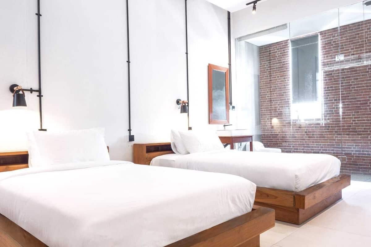 A modern hotel room with two beds, a brick wall, and a large window.