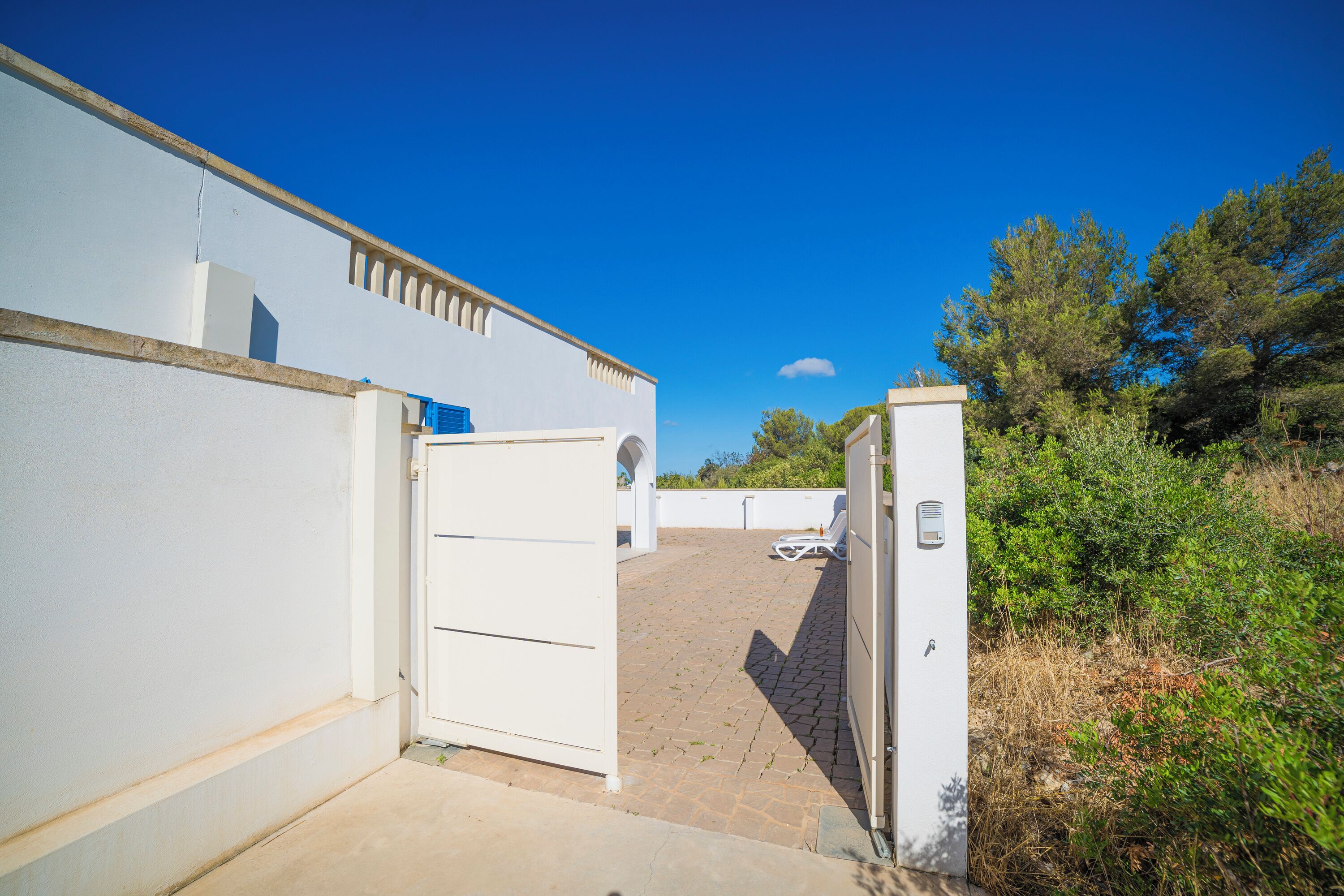 A pathway leading to a white building with a door and a small white structure with a blue roof.