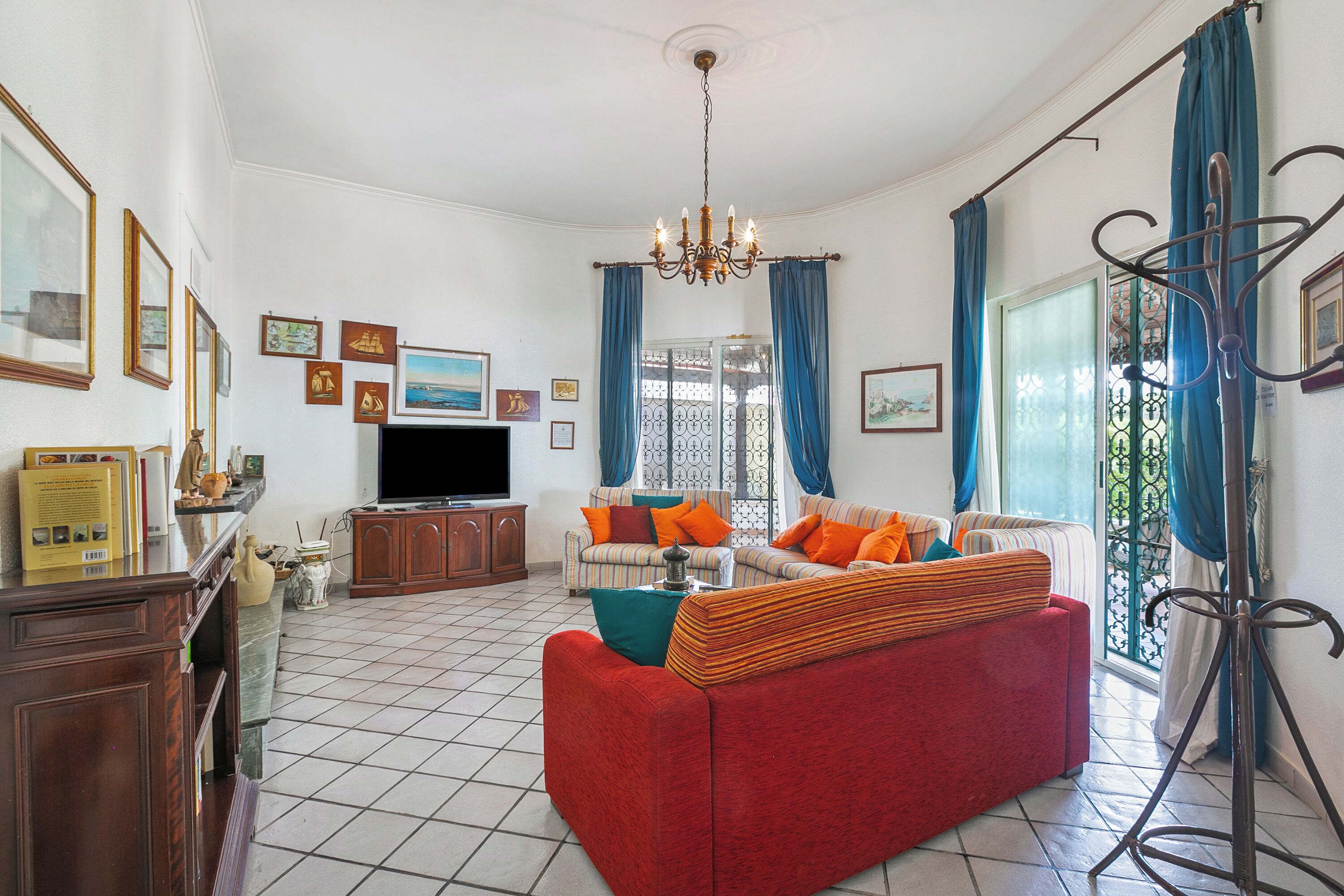 A living room with a red sofa, a television, and a chandelier.