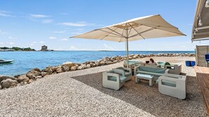 Um terraço à beira-mar com mesas e cadeiras ao ar livre e um grande guarda-sol.