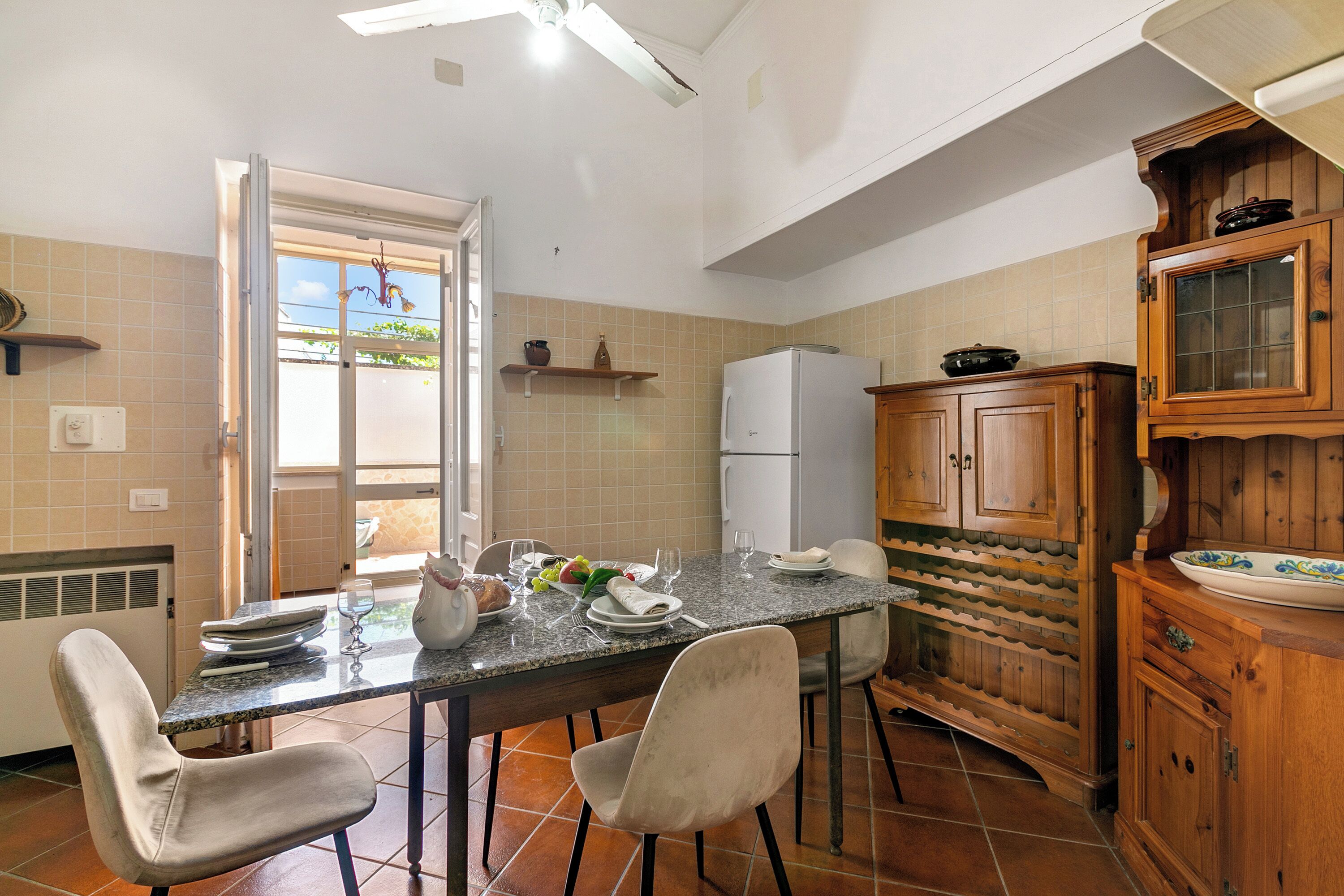 Una cucina con tavolo da pranzo per quattro persone, frigorifero, pensili in legno e una finestra con vista.