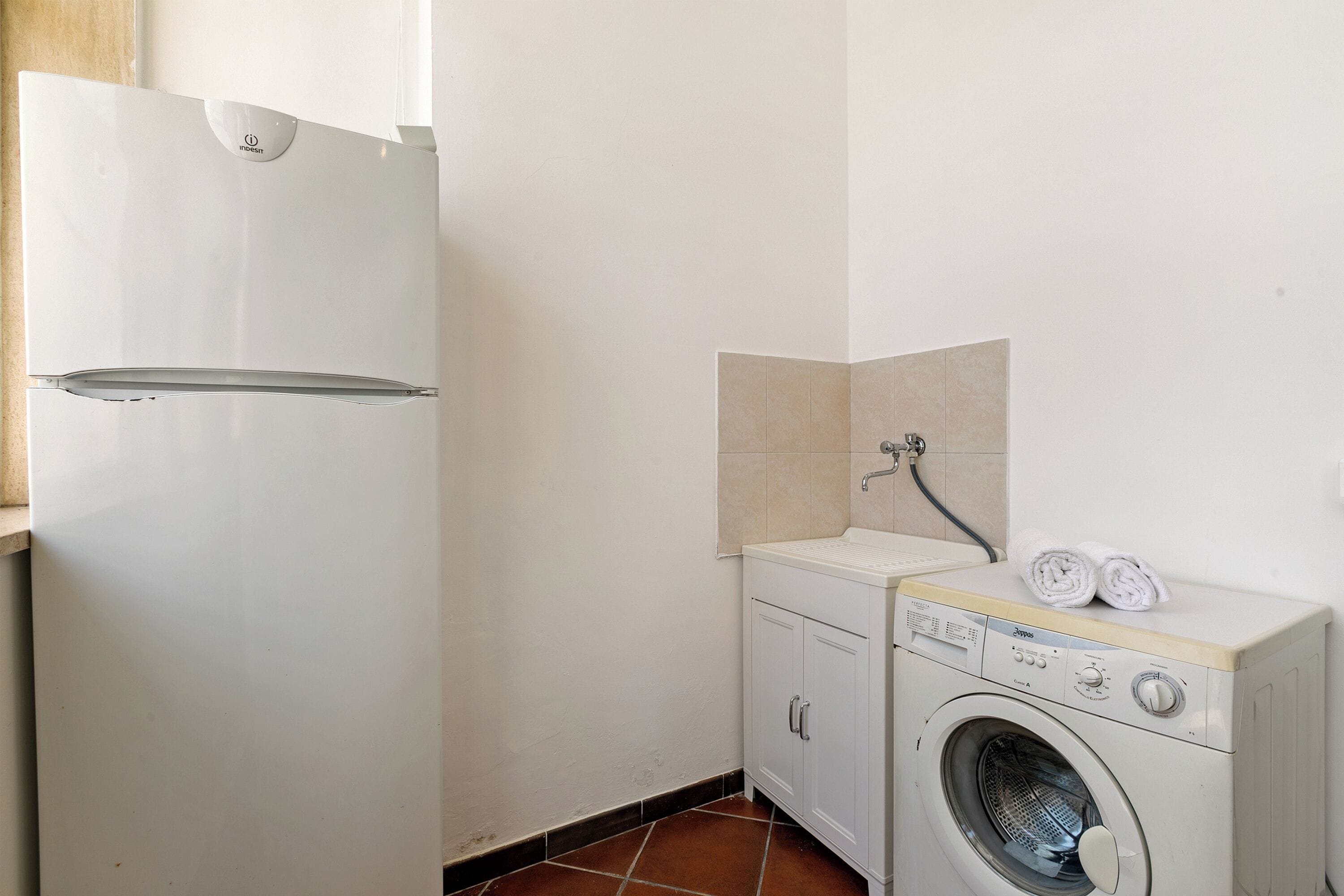 A compact laundry room with a washing machine, a small sink, and a refrigerator.