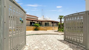 Uma entrada com portão e um pátio com azulejos que levam a um edifício com telhado em azulejos e antena parabólica.