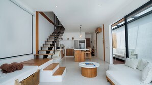 A modern interior with a staircase, a kitchen, a dining area, and a living room with a sofa and coffee table. - Mija Bhuana Agung Villa by Betterplace (Canggu)