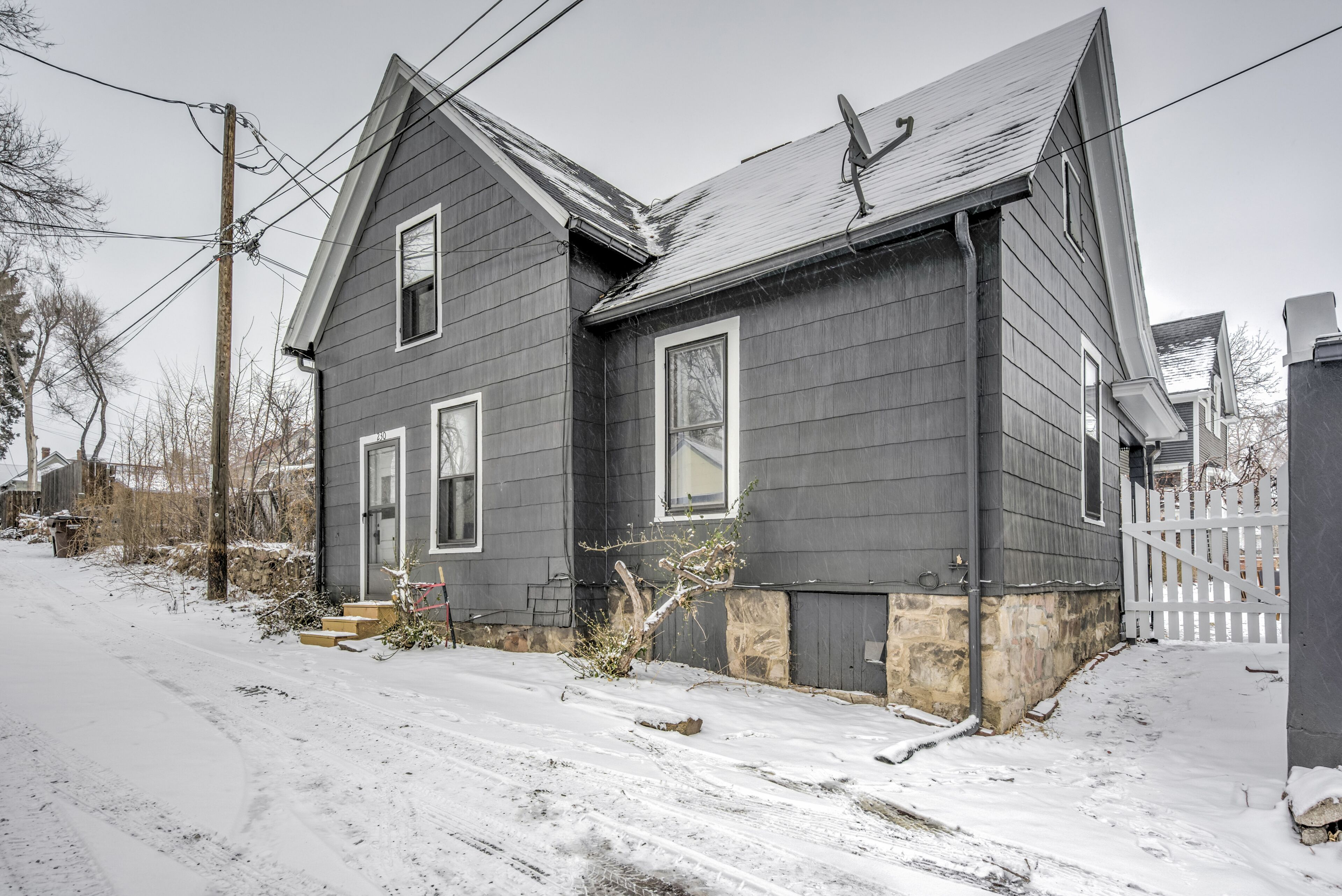 A two-story house with a gray exterior, a front porch, and a snow-covered driveway.