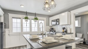 Eine moderne Küche mit weißen Schränken, einer zentralen Kochinsel mit Sitzgelegenheiten, einem Edelstahlkühlschrank und einem eingebauten Backofen.