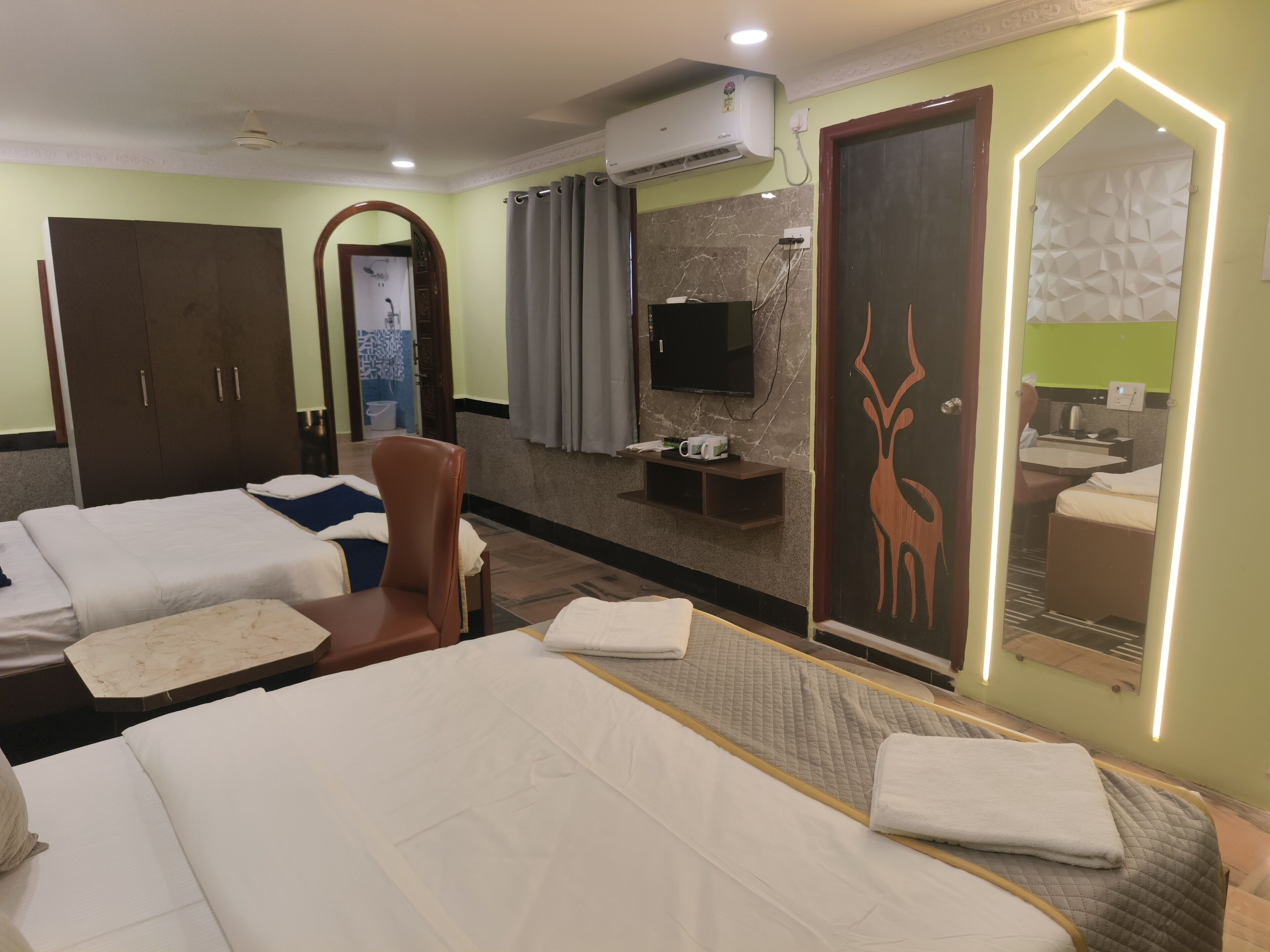 A hotel room with two beds, a TV, a mirror, and a bathroom visible through a door.