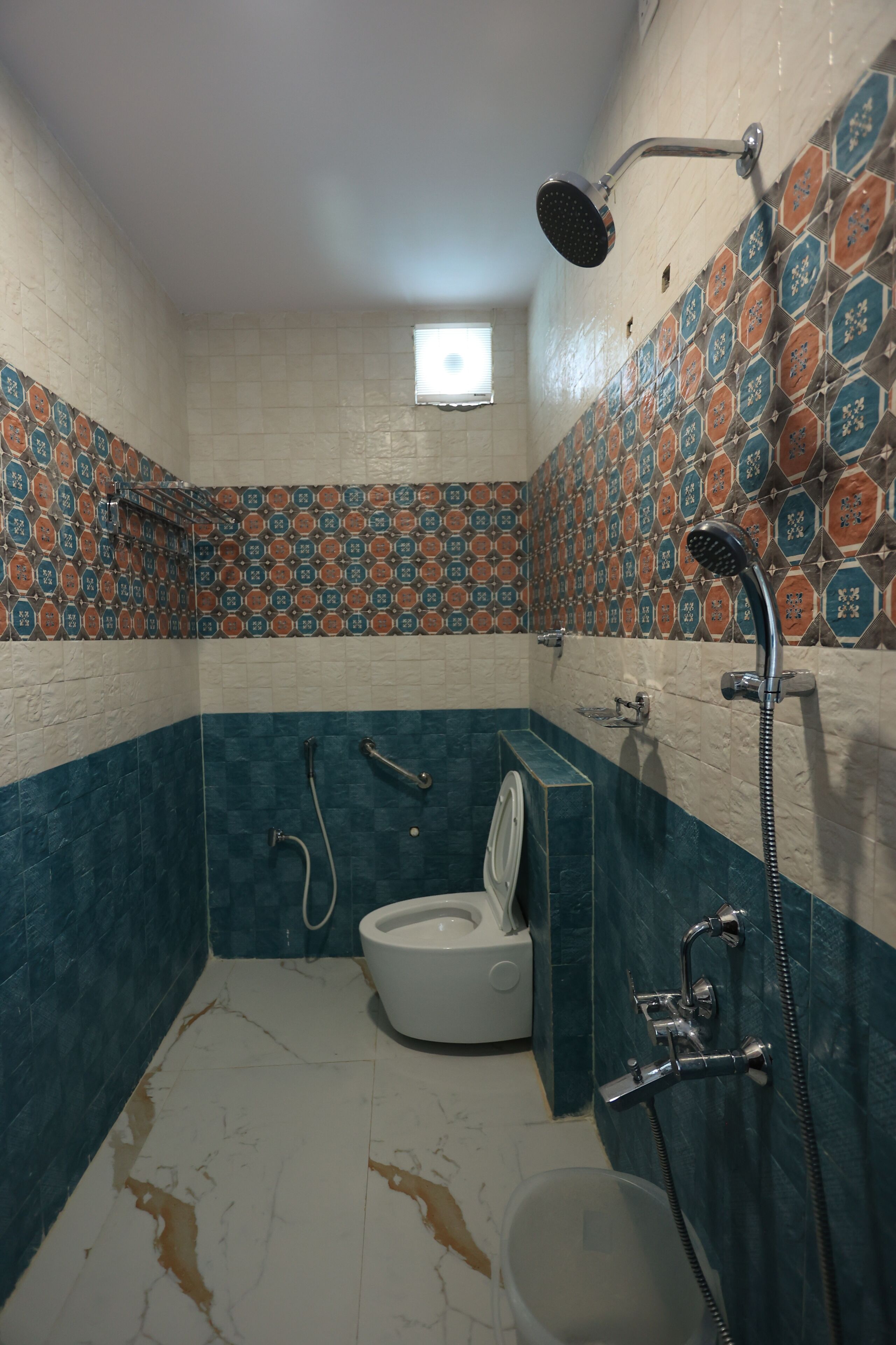 Un baño con inodoro, ducha y pared de baldosas estampadas.