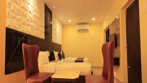 A hotel room with a bed, two red chairs, a small table, and a ceiling fan. - Kailasaa Residency (Tiruvannamalai)