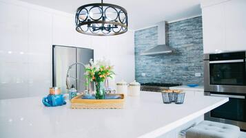 Eine moderne Küche mit weißen Schränken, einer großen Kochinsel, einem Edelstahlbackofen und einer Stein-Spritzschutzwand.