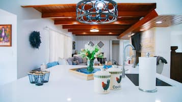 Eine moderne Küche mit weißen Arbeitsflächen, einer Hängeleuchte und einem Essbereich mit einer Couch und einem Couchtisch.