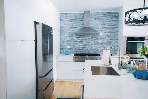 A modern kitchen with white cabinetry, a stainless steel range hood, a blue backsplash, and a built-in oven.