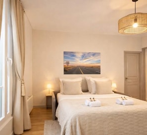 Un dormitorio con una cama, dos lámparas de noche, un cuadro de un camino y una puerta.