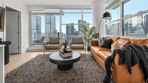 Una sala de estar moderna con un ventanal grande, un sofá de cuero, dos sillones, una mesa de centro y vistas a la ciudad.