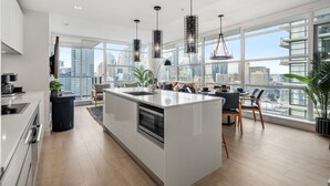 Una cocina moderna con una isla central, ventanas amplias que ofrecen vistas a la ciudad e iluminación colgante contemporánea.